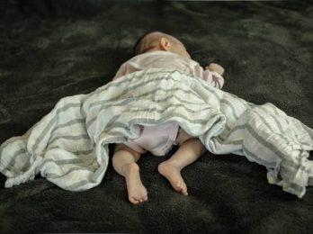 A newborn baby laying on her stomach and with loose bedding. SIDS awareness.